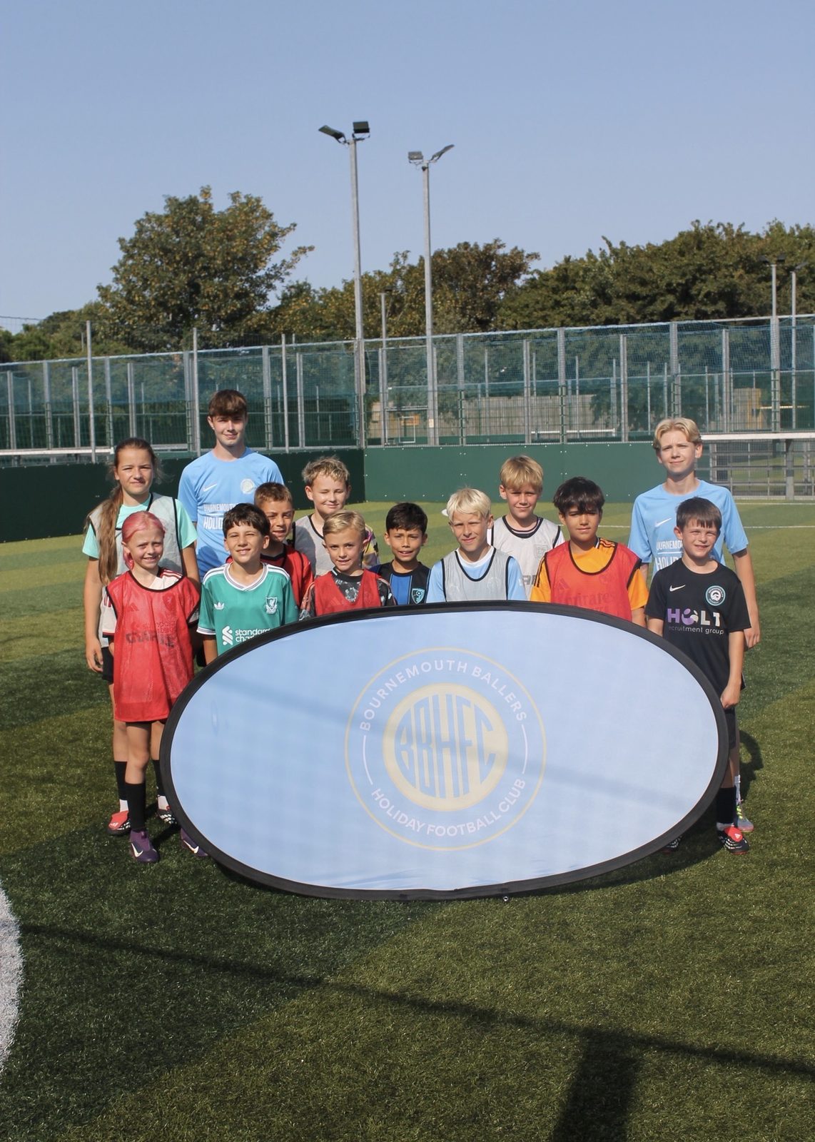 The full camp gathered around the Bournemouth Ballers banner at a summer holiday football camp, Pelhams Park