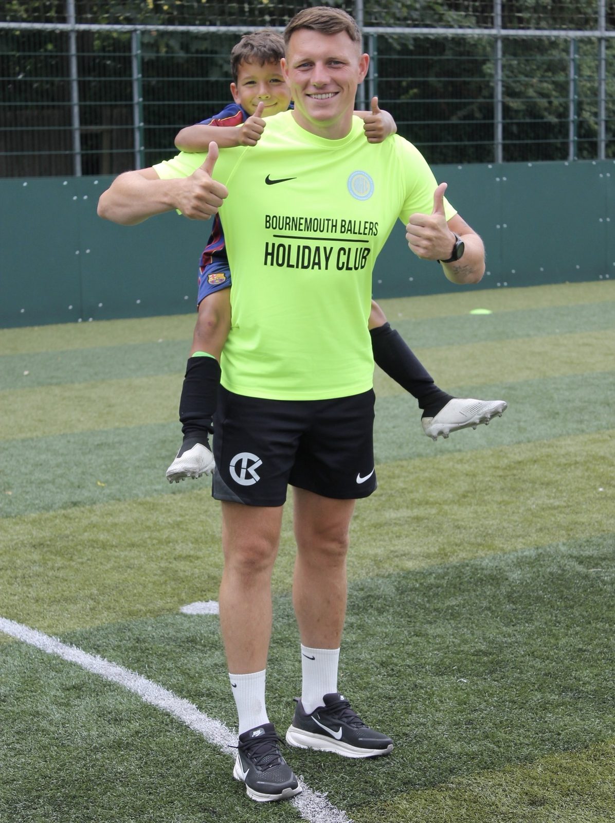 A Bournemouth Ballers coach giving a thumbs up with a young player on his shoulders